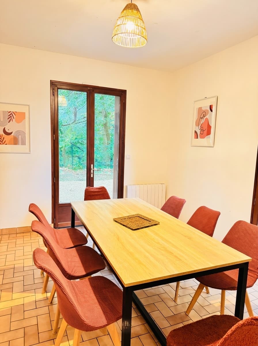 Salle à manger lumineuse avec table en bois et chaises terracotta, ouvrant sur le jardin du gîte